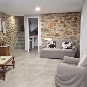 Sala de estar de Casa engracia donde se pueden ver las paredes rústicas de piedra, las escaleras de acceso a la planta superior y el mobiliario, incluidos varios sofás y sillones
